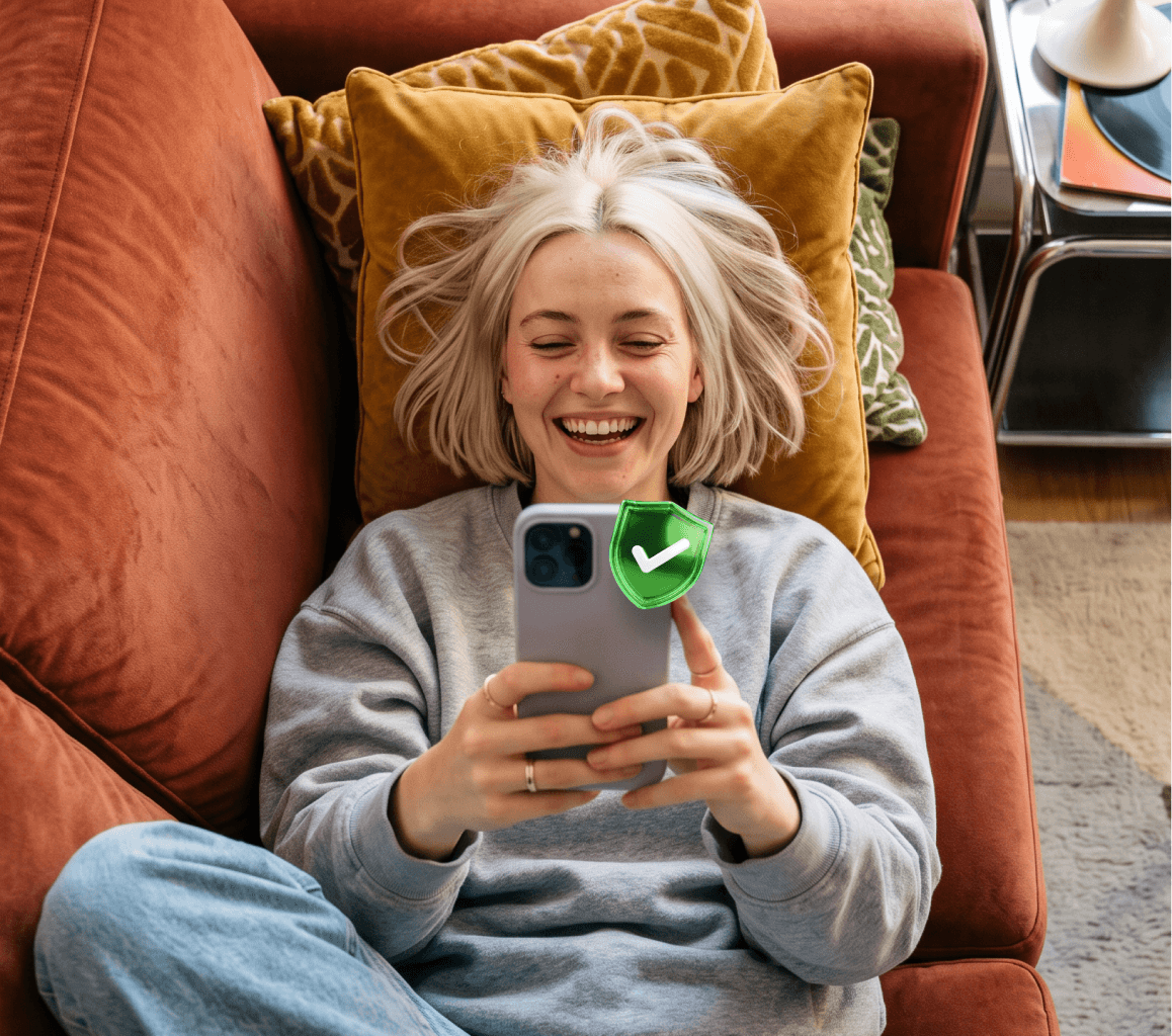 Femme souriante assise sur un canapé, un téléphone à la main.